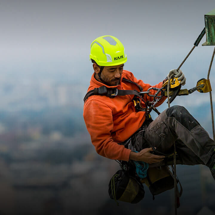 A technical professional is working at height performing building maintenance. He is secured by a rope and wearing a KASK helmet.